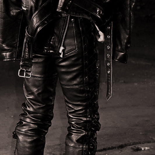 Person wearing black leather pants and boots in a dark setting