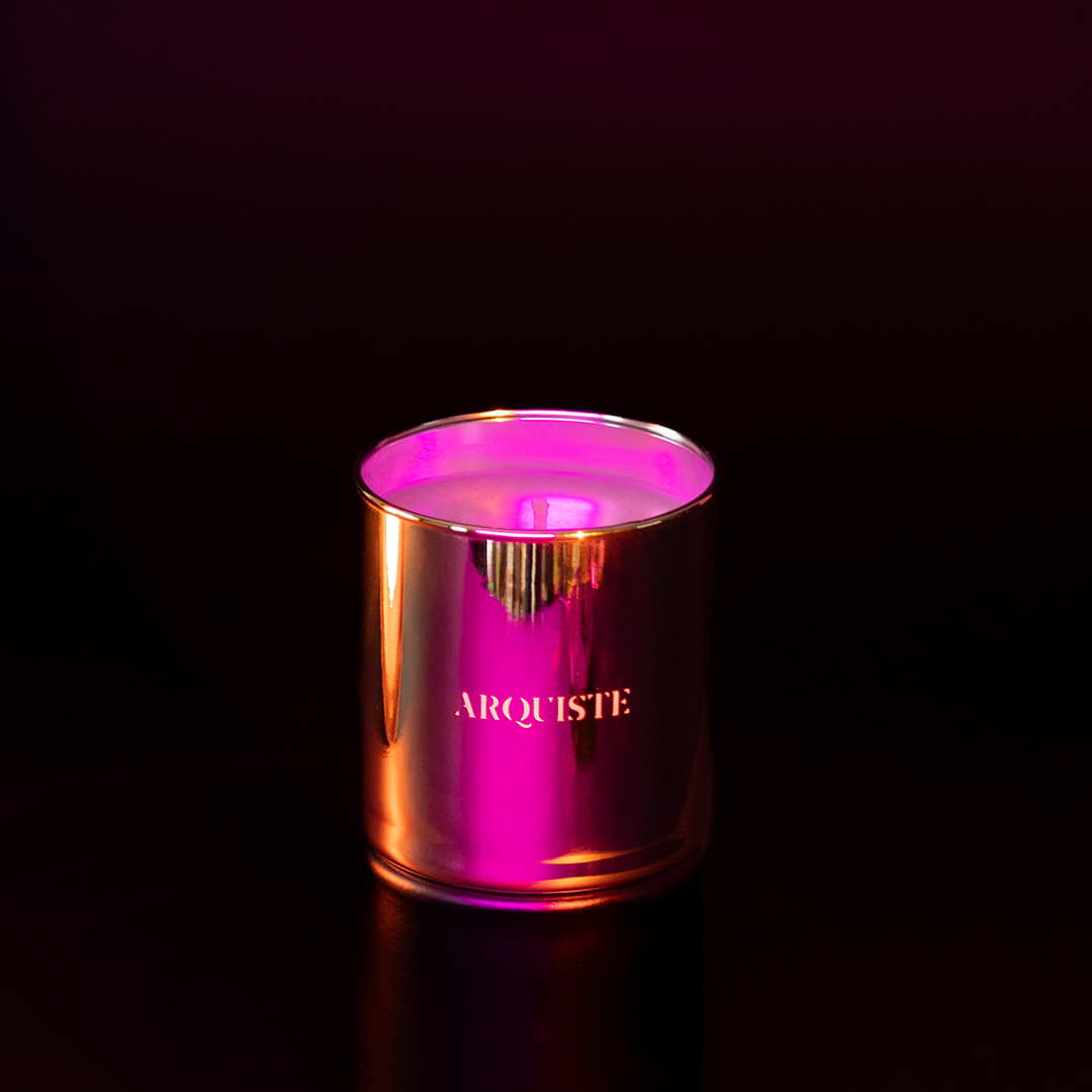 A metallic rose gold candle jar with the brand name 'ARQUISTE' on the front, glowing with a vibrant pink neon light against a dark background.
