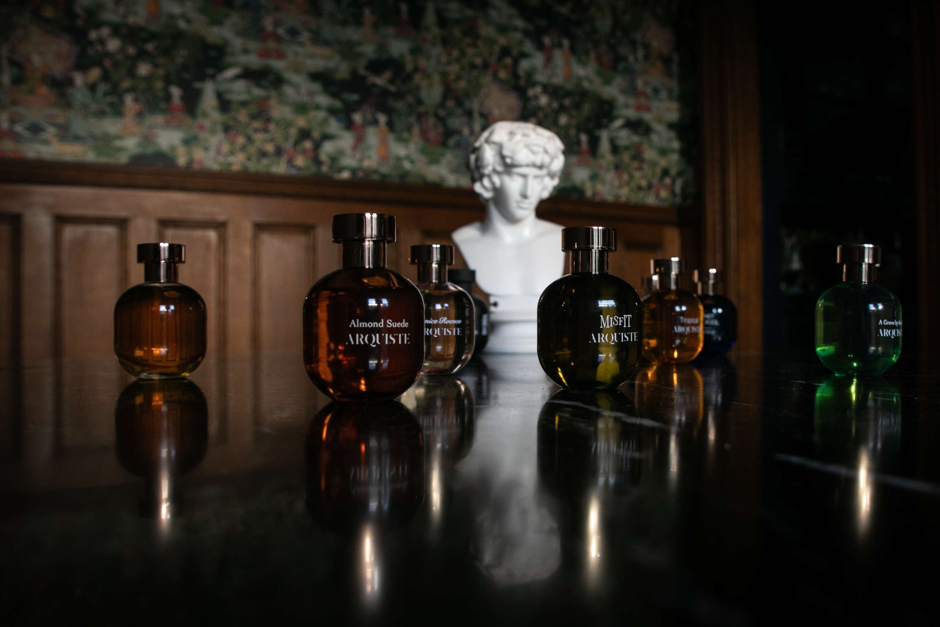 Collection of perfume bottles on a reflective surface with a classical bust in the background
